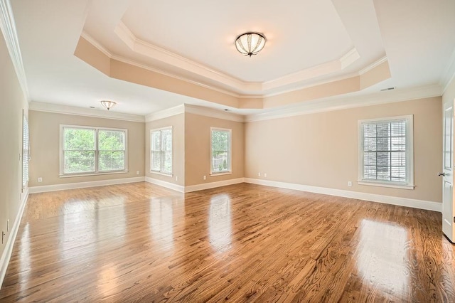 unfurnished living room with crown molding, baseboards, a raised ceiling, and wood finished floors