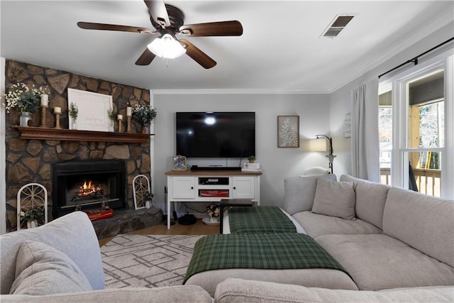 living area with a stone fireplace, crown molding, wood finished floors, and visible vents