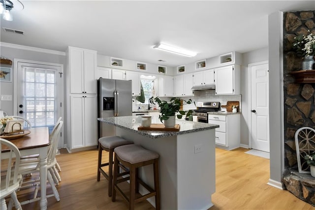 kitchen featuring tasteful backsplash, visible vents, under cabinet range hood, light wood-type flooring, and stainless steel appliances