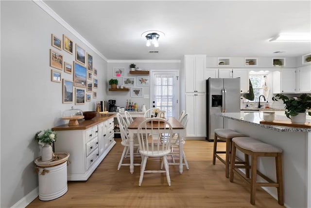 dining space with light wood-type flooring, baseboards, visible vents, and crown molding