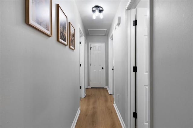 hallway with attic access, light wood-type flooring, and baseboards