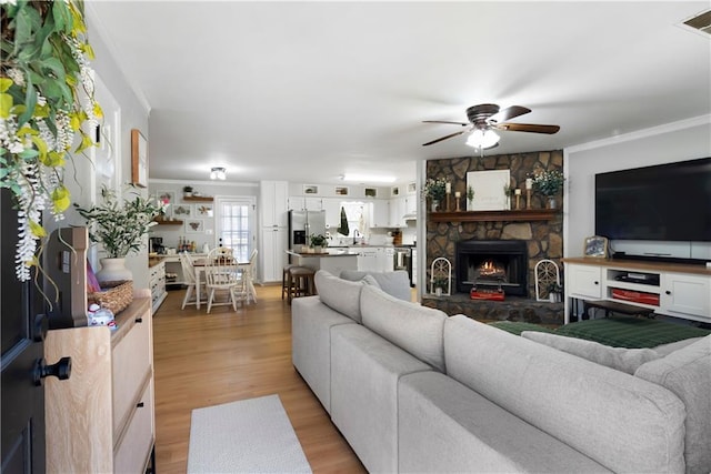 living room featuring ceiling fan, light wood-type flooring, ornamental molding, and a fireplace