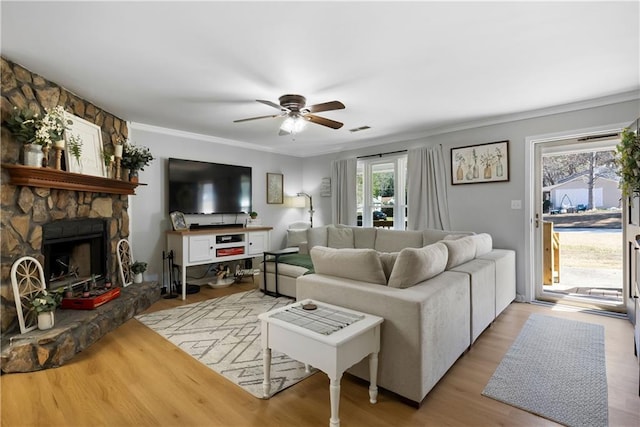 living area with visible vents, crown molding, a stone fireplace, wood finished floors, and a ceiling fan