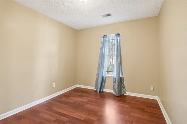 empty room with dark wood-type flooring and a textured ceiling