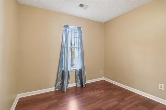 spare room featuring a textured ceiling and dark hardwood / wood-style floors