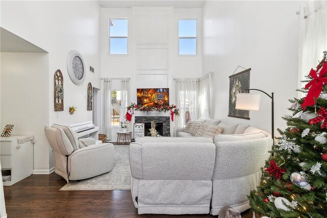 living room featuring a fireplace, a towering ceiling, and dark wood-type flooring