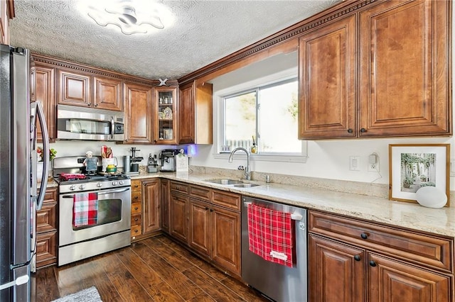 kitchen with sink, light stone counters, dark hardwood / wood-style flooring, a textured ceiling, and appliances with stainless steel finishes