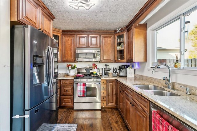 kitchen with light stone countertops, a textured ceiling, stainless steel appliances, dark wood-type flooring, and sink