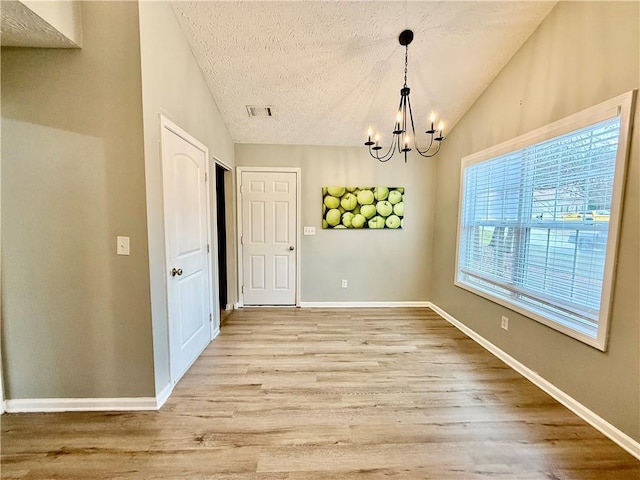 unfurnished dining area with lofted ceiling, a textured ceiling, a chandelier, and light wood-type flooring