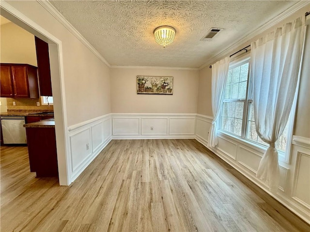 unfurnished dining area featuring ornamental molding, a textured ceiling, and light wood-type flooring