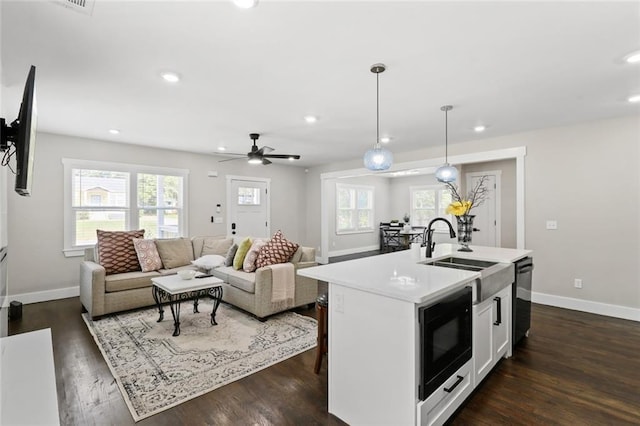 kitchen with black microwave, a kitchen island with sink, dark wood-type flooring, sink, and decorative light fixtures