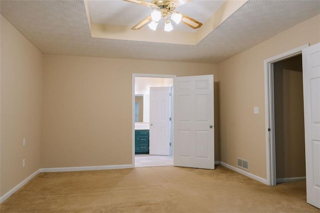 spare room featuring light carpet, ceiling fan, a tray ceiling, and a textured ceiling