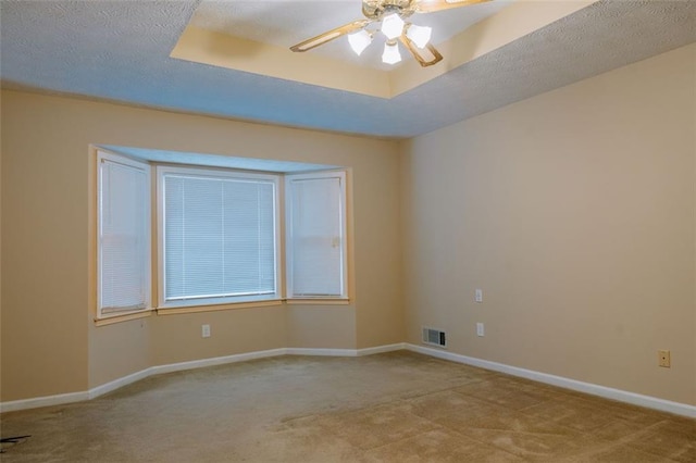 carpeted spare room featuring ceiling fan, a textured ceiling, and a tray ceiling