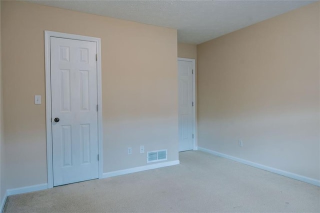 spare room featuring light colored carpet and a textured ceiling