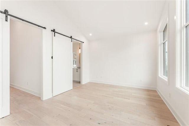 empty room featuring a barn door, lofted ceiling, and light wood-type flooring