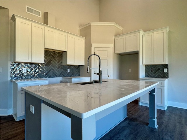 kitchen featuring a center island with sink, a sink, visible vents, and white cabinetry