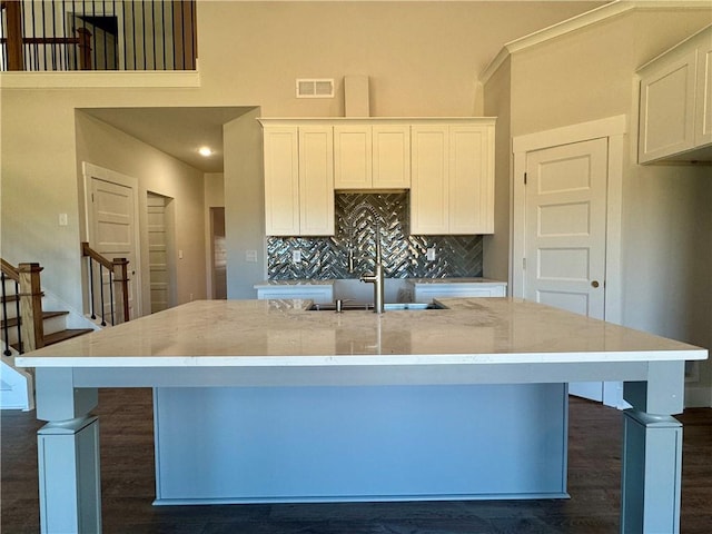 kitchen with a sink, visible vents, white cabinetry, decorative backsplash, and an island with sink