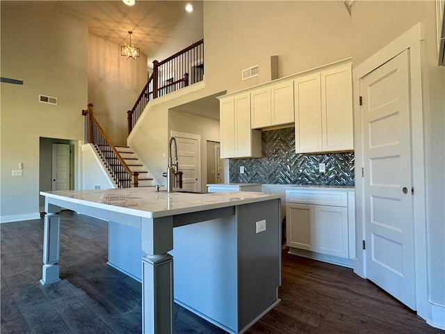 kitchen featuring a kitchen island with sink, a sink, visible vents, and white cabinetry