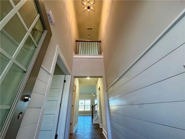 hallway with baseboards, a high ceiling, visible vents, and wood finished floors