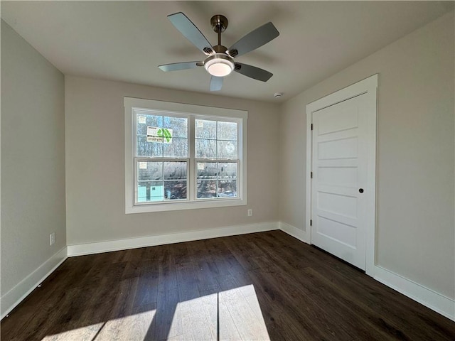 spare room featuring ceiling fan, dark wood-type flooring, and baseboards