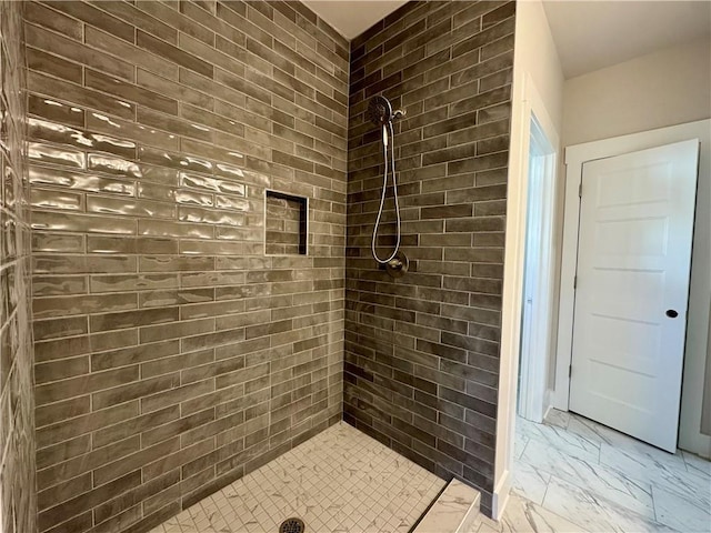 bathroom with marble finish floor and a tile shower