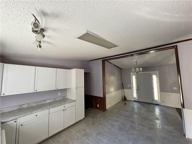 kitchen featuring wooden walls, a textured ceiling, decorative light fixtures, white cabinetry, and a chandelier