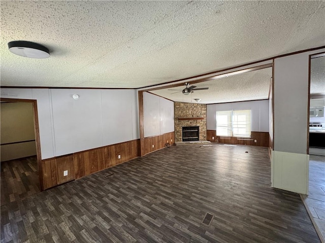 unfurnished living room featuring dark wood-type flooring, crown molding, a brick fireplace, ceiling fan, and a textured ceiling