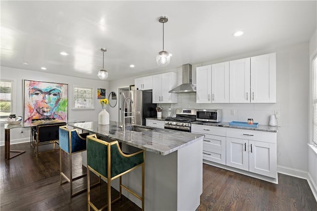 kitchen featuring stainless steel appliances, white cabinetry, wall chimney range hood, and an island with sink