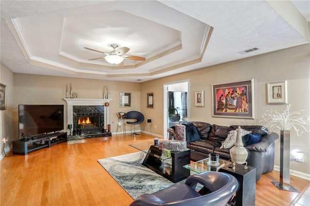 living room with ceiling fan, hardwood / wood-style flooring, a tray ceiling, and ornamental molding