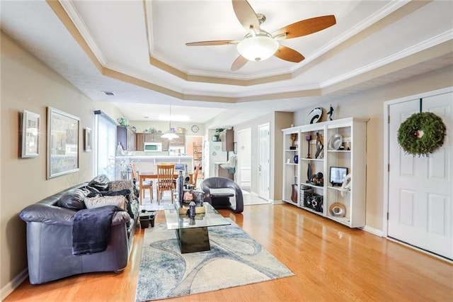 living room with ceiling fan, crown molding, light hardwood / wood-style flooring, and a raised ceiling