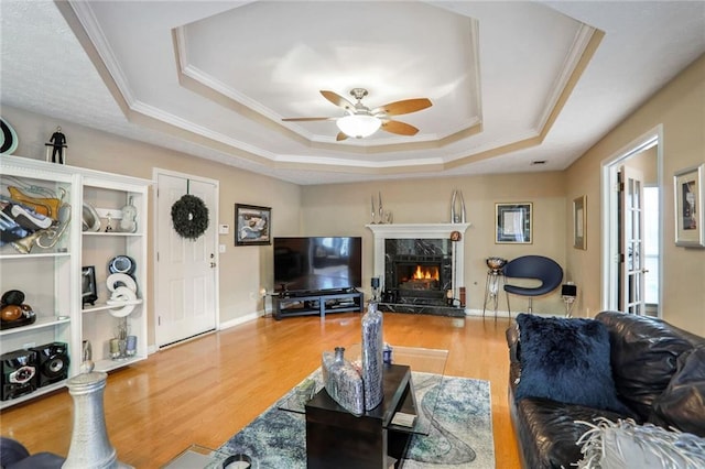 living room featuring ceiling fan, a raised ceiling, wood-type flooring, a premium fireplace, and ornamental molding