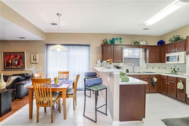 kitchen with white appliances, sink, backsplash, hanging light fixtures, and a breakfast bar