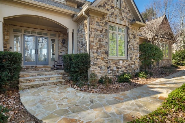 entrance to property with stone siding, french doors, and roof with shingles