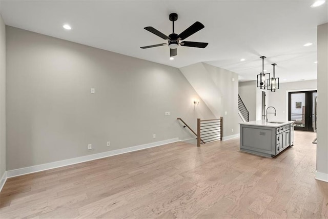 unfurnished living room with ceiling fan with notable chandelier, light hardwood / wood-style flooring, and sink