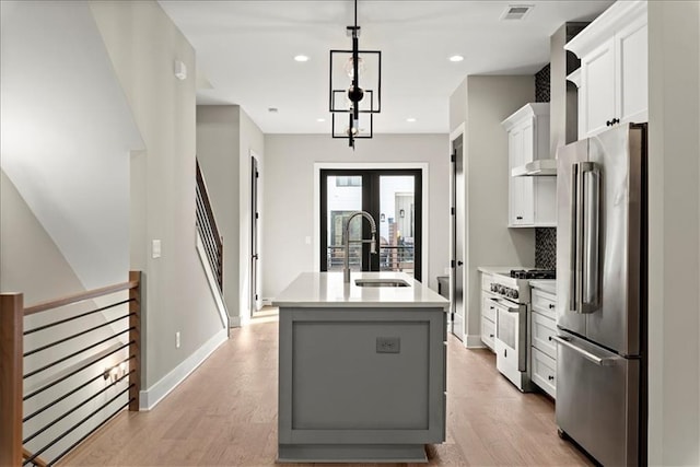 kitchen with premium appliances, sink, pendant lighting, white cabinetry, and an island with sink