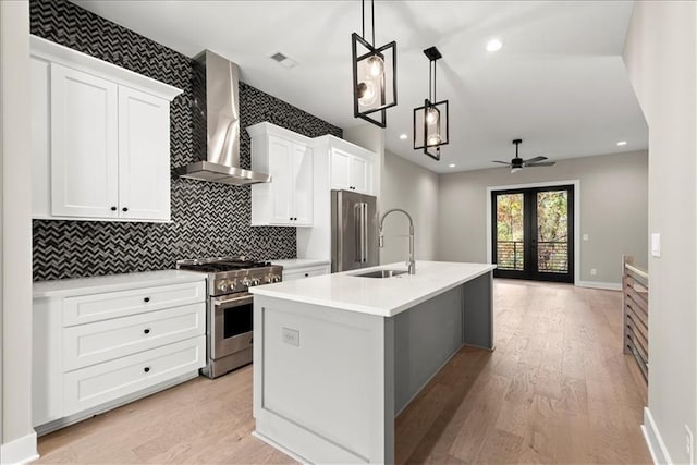 kitchen featuring ceiling fan, hanging light fixtures, wall chimney range hood, a kitchen island with sink, and high end appliances