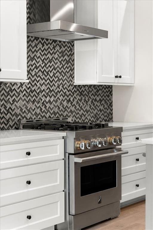 kitchen featuring backsplash, stainless steel stove, white cabinetry, and wall chimney range hood