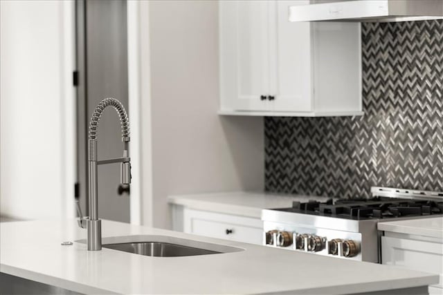 kitchen with sink, stainless steel range, ventilation hood, backsplash, and white cabinets