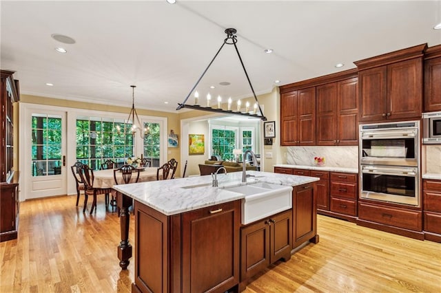 kitchen featuring light wood finished floors, tasteful backsplash, crown molding, stainless steel appliances, and a kitchen island with sink