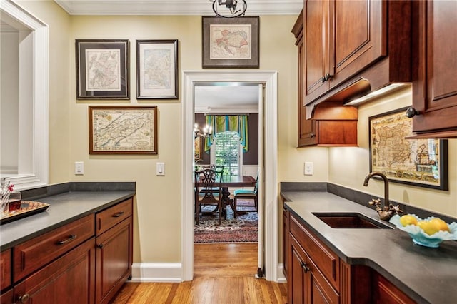 kitchen with a sink, dark countertops, crown molding, and light wood finished floors