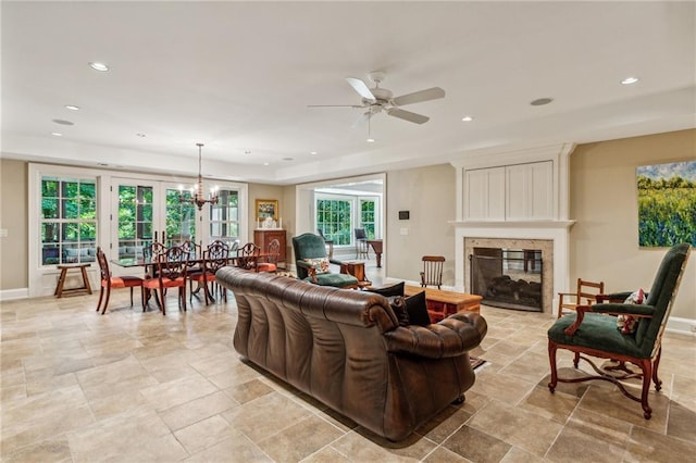 living room featuring baseboards, recessed lighting, a fireplace, stone finish flooring, and ceiling fan with notable chandelier