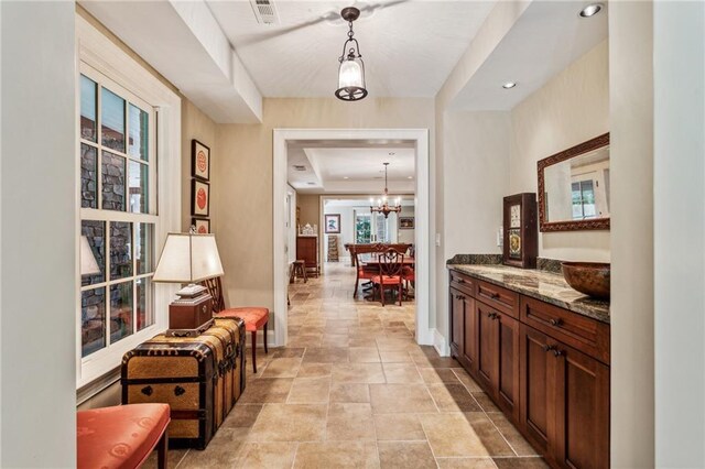 corridor featuring baseboards, visible vents, recessed lighting, stone finish flooring, and a chandelier