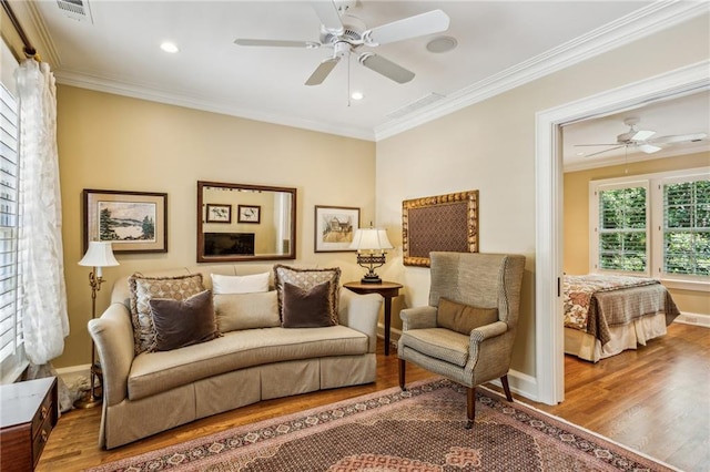 living area with wood finished floors, a ceiling fan, and crown molding