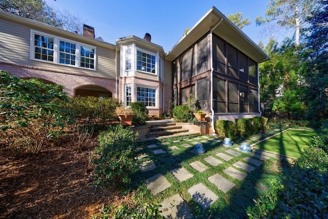 back of property with brick siding, a chimney, and a sunroom