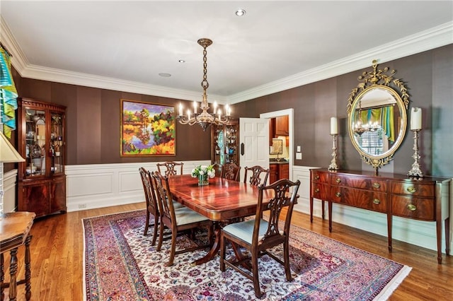 dining space with a wainscoted wall, an inviting chandelier, wood finished floors, and ornamental molding