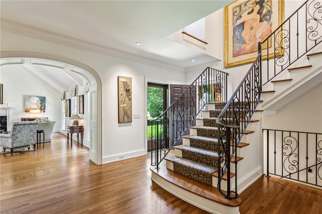 interior space with baseboards, arched walkways, wood finished floors, and crown molding