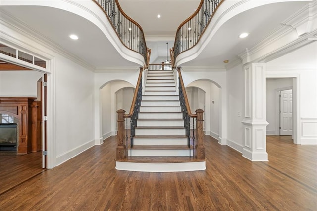 stairs with arched walkways, wood finished floors, and ornamental molding