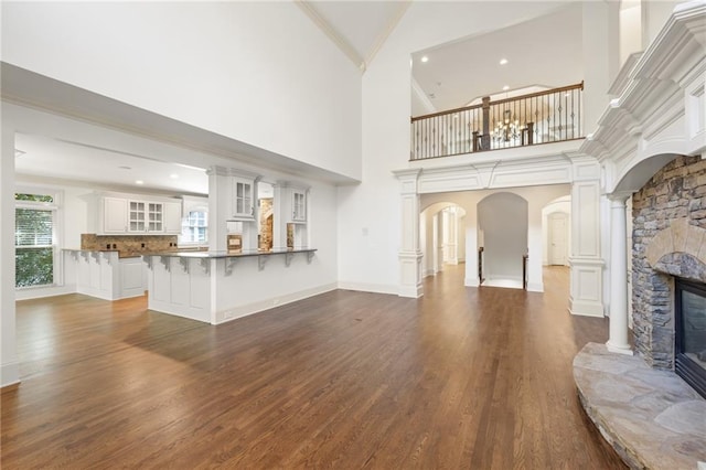 living room with a stone fireplace, dark wood finished floors, decorative columns, and crown molding