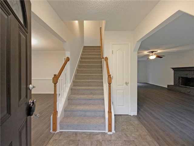 stairway featuring hardwood / wood-style floors, a textured ceiling, a brick fireplace, and ceiling fan