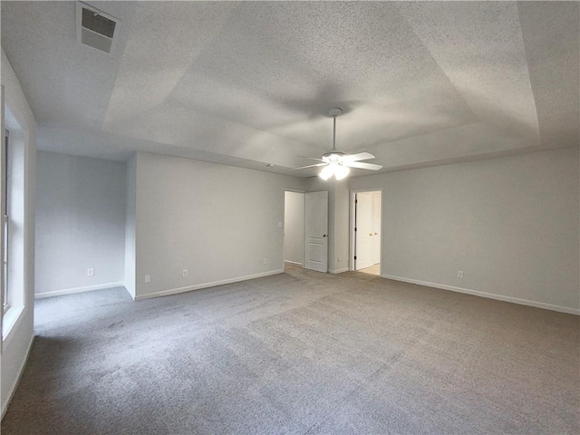 unfurnished room with a raised ceiling, ceiling fan, carpet, and a textured ceiling